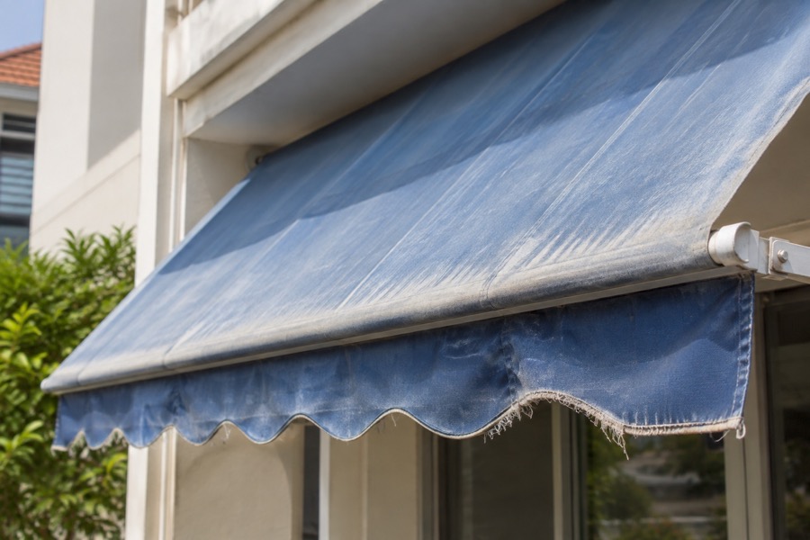 Close-up of faded blue awning cover with lightly frayed valance, intact supporting edge, illustrates worn fabric only