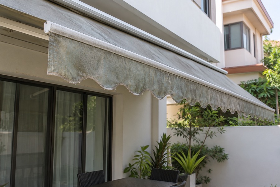 Faded grey retractable awning with worn fabric and frayed valance