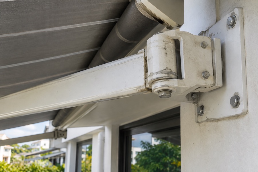 Close-up of a folding-arm awning pivot joint and bracket showing ordinary wear on painted metal