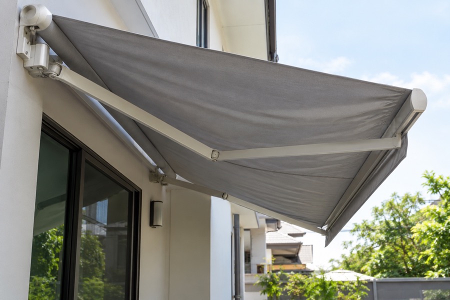 Retractable awning seen from below with slightly uneven fabric tension, modest residential wall, illustrative assessment subject