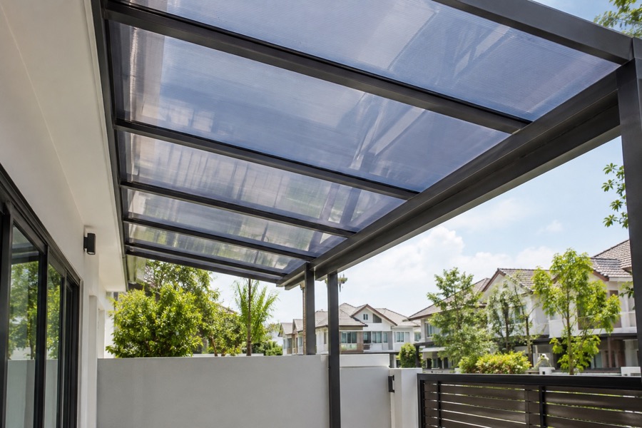 Under-roof view of tinted polycarbonate panels on a simple porch frame, natural daylight filtering through, clear support detail
