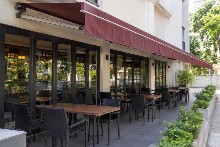 Empty simple restaurant outdoor seating under a burgundy fabric awning, side-on architectural view