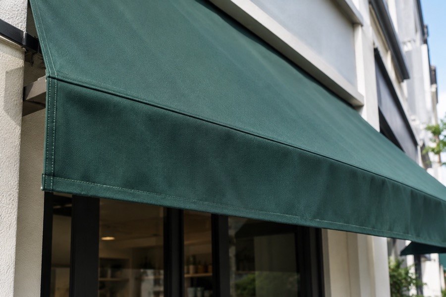 Close-up of taut woven dark green canopy fabric and a clean straight valance edge above a modest shopfront, focus on material