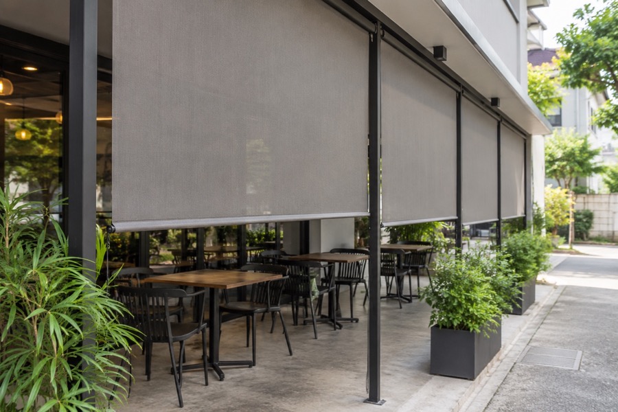 Empty neighbourhood café side seating area screened by ordinary vertical outdoor roll-down blinds