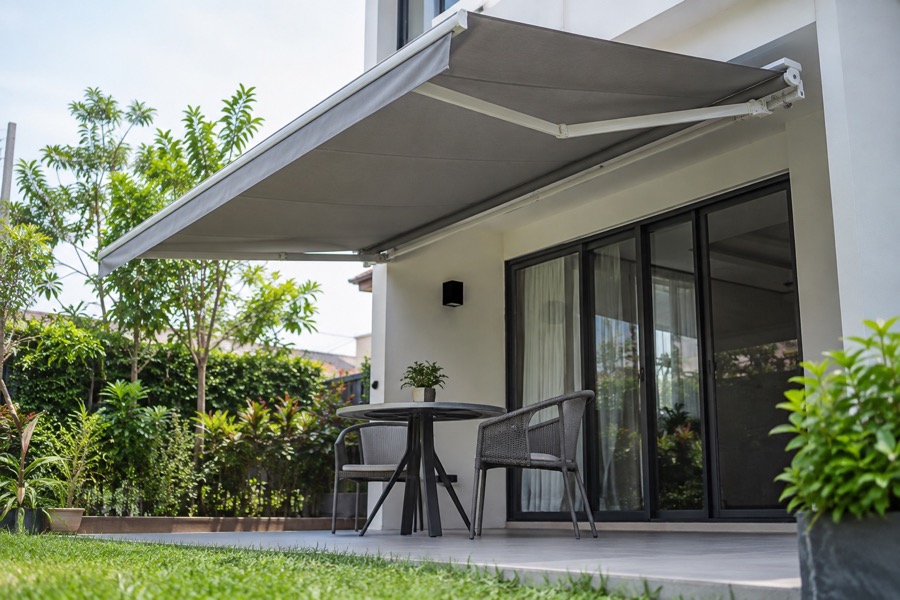 Low-angle garden view of a grey retractable awning shading an empty patio chair and simple table, focus on usable outdoor space