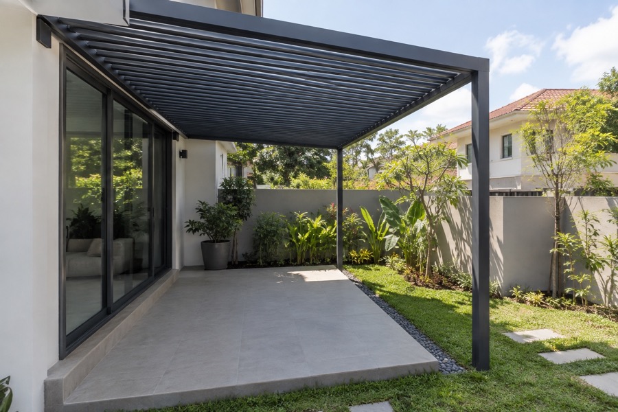 Compact aluminium louvre shade structure over a small empty garden patio, soft sunlight and ordinary home exterior