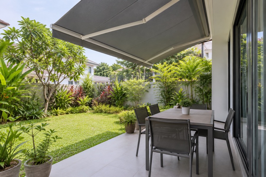 View from a modest tiled patio into a planted garden beneath a simple canopy edge, calm practical outdoor living